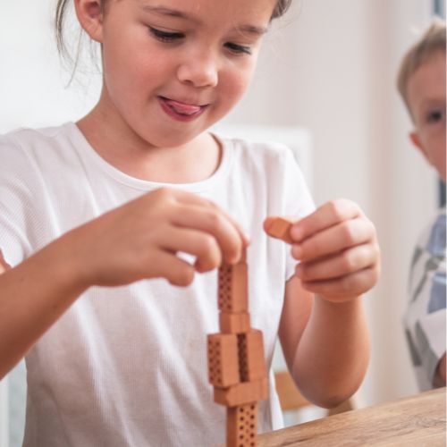 Mädchen stapelt Mini Ziegelsteine zu einem Turm und trainiert so ihre Feinmotorik.